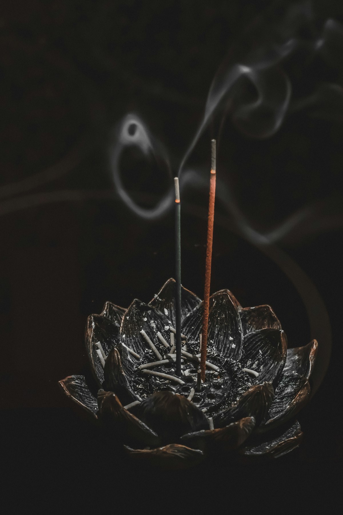 Incense sticks burning in a lotus holder, smoke curling in the dark