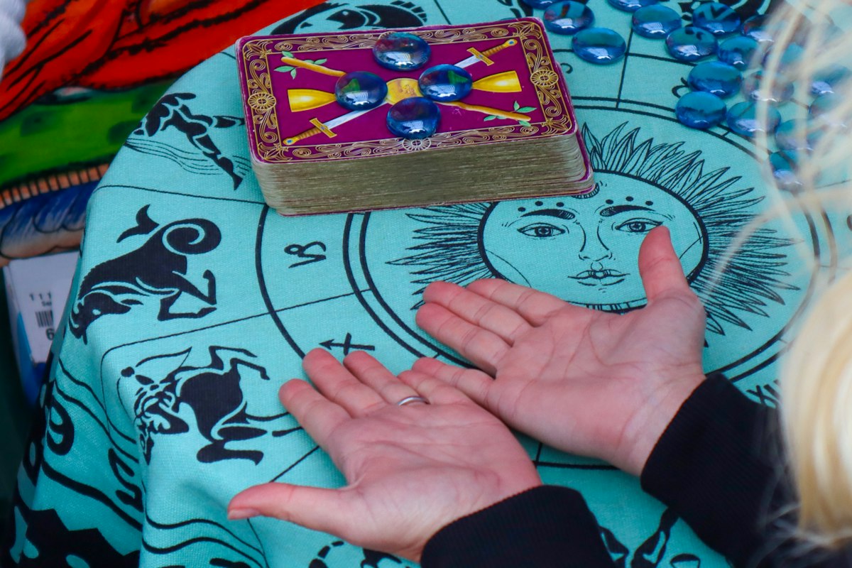 Open palms resting on a zodiac reading cloth beside a tarot deck